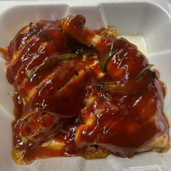 Marie's Soul Food BBQ chicken, smothered in rich, dark red sauce, in a white takeout container.