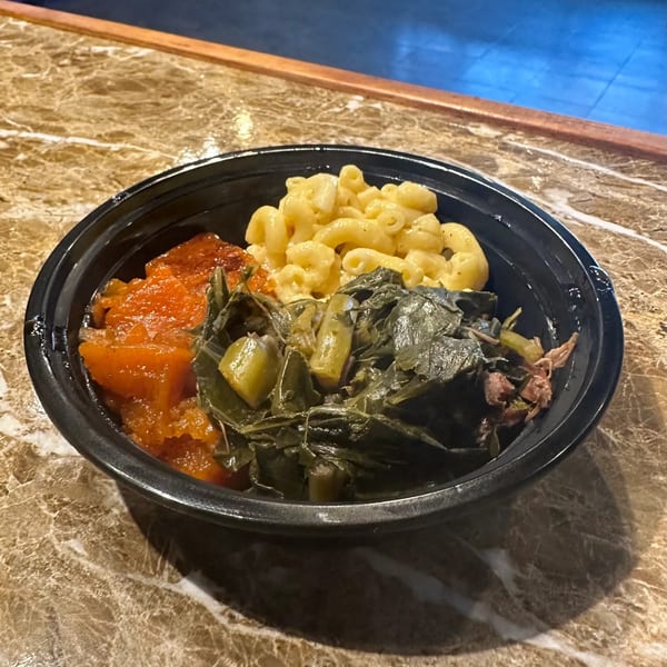 A black bowl of Marie's Soul Food with macaroni and cheese, candied yams, and collard greens.
