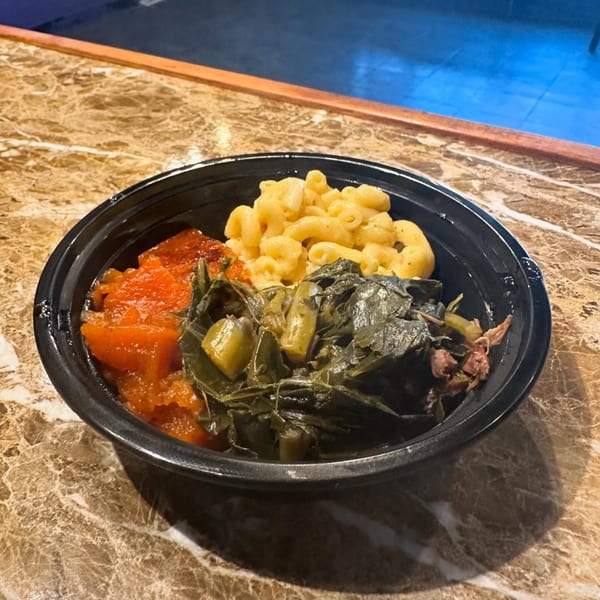 A black bowl of Marie's Soul Food with macaroni and cheese, candied yams, and collard greens.